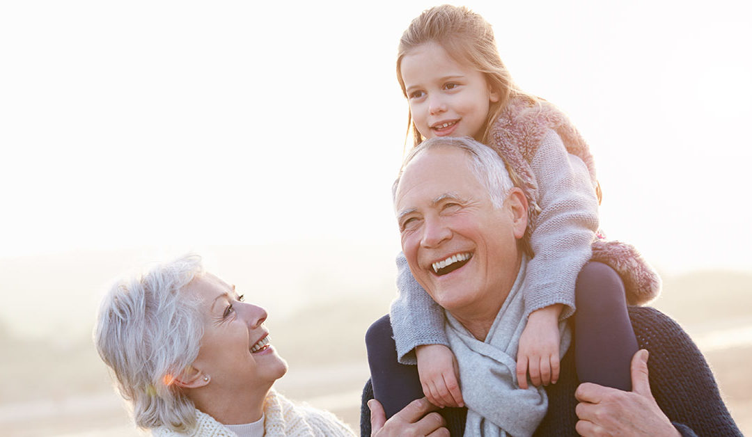 Großeltern lachen mit Enkelin auf den Schultern des Opas am Strand | Immobilienverrentung