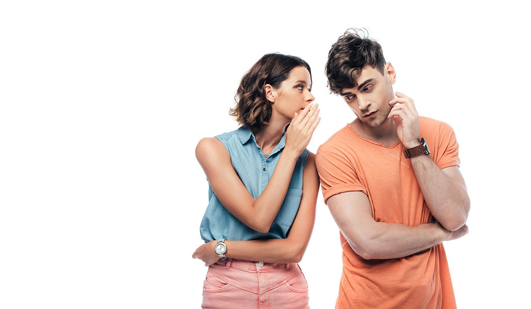 Eine junge Frau flüstert einem jungen Mann etwas ins Ohr als Symbolbild für diskreten Immobilienverkauf | Immobilienverkauf