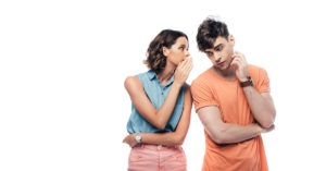 Eine junge Frau flüstert einem jungen Mann etwas ins Ohr als Symbolbild für diskreten Immobilienverkauf | Immobilienverkauf